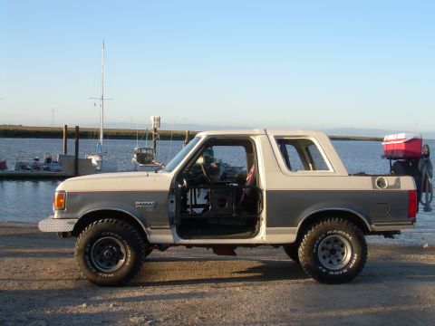 1991 Ford Bronco - Side view of a 1991 Ford Bronco with its doors open, parked near a waterfront.