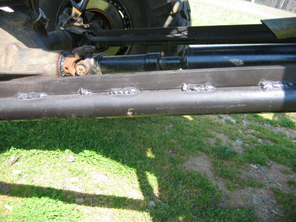 Vehicle undercarriage with visible welds on a metal tube, part of a driveshaft and suspension visible