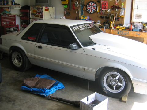 1992 Ford Mustang - A white 1992 Ford Mustang coupe is parked in a garage, showing its aftermarket hood scoop and racing tires.