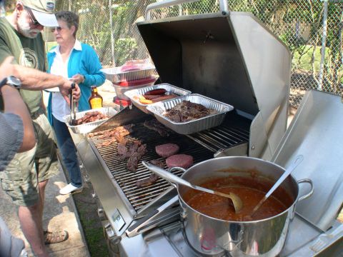 2007 Toyota FJ Cruiser - A group of people are gathered around a grill, cooking various meats and hot dogs for a meal.