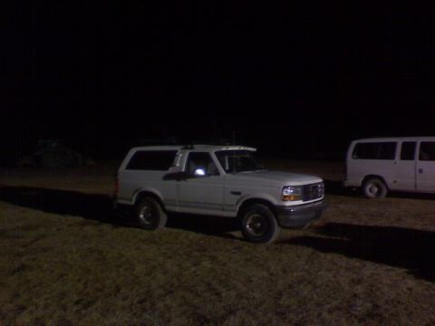 1995 Ford Bronco - White Ford Bronco and a white van are parked on a grassy area at night.