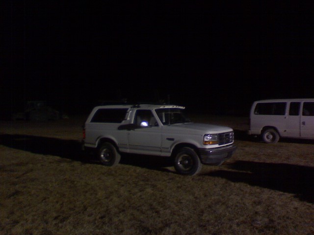 1995 Ford Bronco parked at night next to a white van