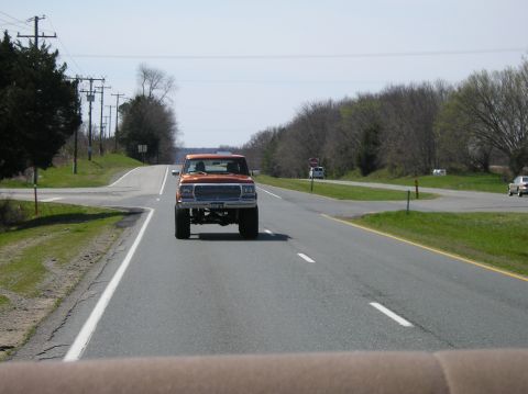 1993 Ford Bronco - Lifted orange pickup truck seen from inside another vehicle on a highway.