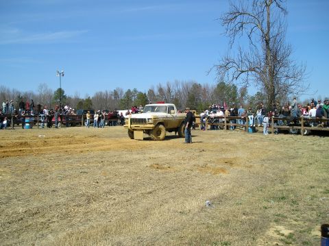1993 Ford Bronco - A crowd watches as a lifted Ford pickup truck sits in a dirt field under a clear blue sky.