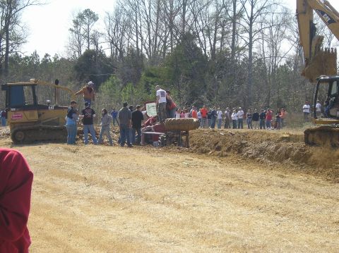 1993 Ford Bronco - An off-road event shows a red SUV overturned in a dirt pit, with heavy machinery and spectators present.