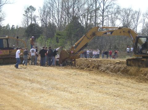 1993 Ford Bronco - An excavator is used to lift a car out of a ditch while a crowd of people observes the scene.