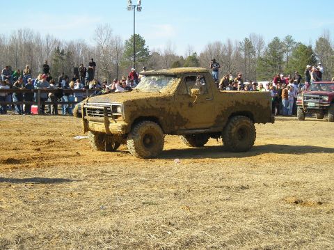 1993 Ford Bronco - Muddy pickup truck competes in an event with spectators watching from behind a fence.