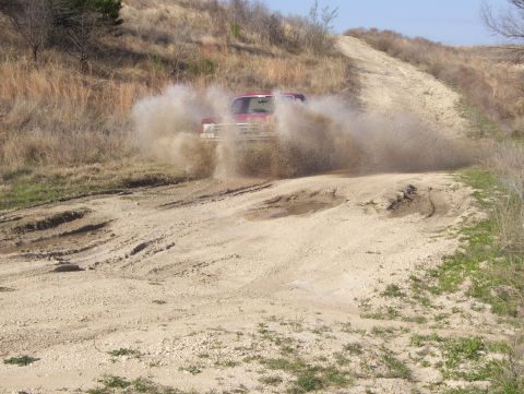 1988 Ford Bronco - A red pickup truck powers through a muddy obstacle on a dirt track, off-road path.