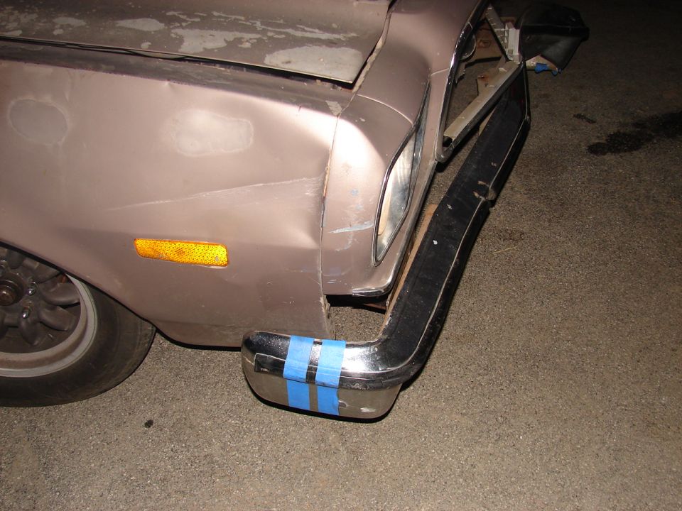 Loose chrome front bumper taped with blue tape hanging off a tan car's dented front corner