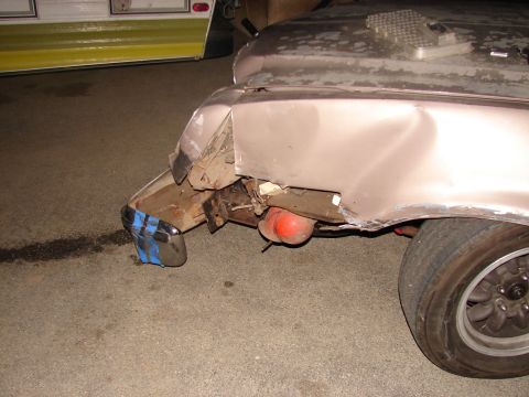 1973 Ford Ranchero - Close-up of heavy collision damage on the corner of a tan/beige car: the fender and valance are crumpled and torn open, and a chrome bumper…