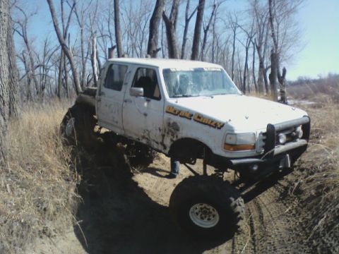1992 Ford F-350 - A white pickup truck navigates a muddy, wooded trail with its tires deep in the dirt.