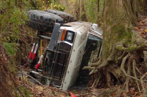 1979 Ford Bronco - White SUV overturned in a ditch, surrounded by trees and foliage.
