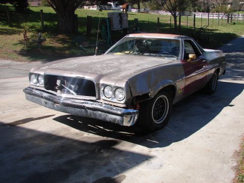 1973 Ford Ranchero - Front three-quarter view of a weathered early-1970s Ford Ranchero project in faded tan and primer with a mismatched maroon door and quarter…