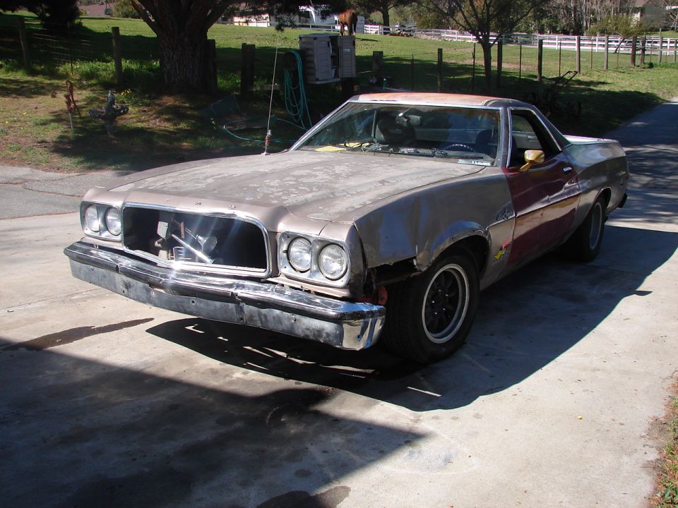 Weathered tan-and-maroon 1970s Ford Ranchero project parked on a rural driveway, front three-quarter view
