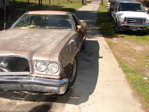 1973 Ford Ranchero - A tan/gold 1970s Ford Ranchero-style car-pickup sits on a concrete driveway as a project, with faded peeling paint, surface rust on the roo…