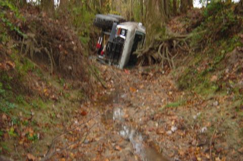 1979 Ford Bronco - An off-road vehicle has overturned and landed on its side in a muddy, wooded area.