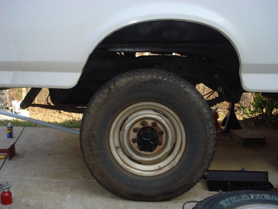 Rear wheel and white-spoke steel wheel of a white pickup truck on jack stands