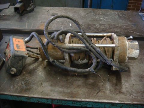 1996 Ford Bronco - Worn winch with coiled cable and electrical conduit on a workbench.