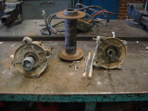 1996 Ford Bronco - Disassembled winch components, including a drum and motor housings, are laid out on a cluttered workbench.