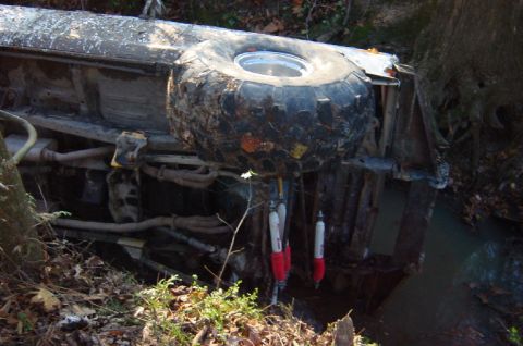 1979 Ford Bronco - Vehicle overturned in a ditch, showing a large spare tire and suspension components.