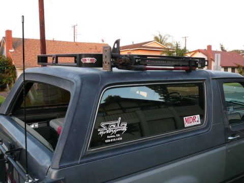 1988 Ford Bronco - This dark gray SUV features a roof rack equipped with tools, suggesting it is ready for off-road adventures.