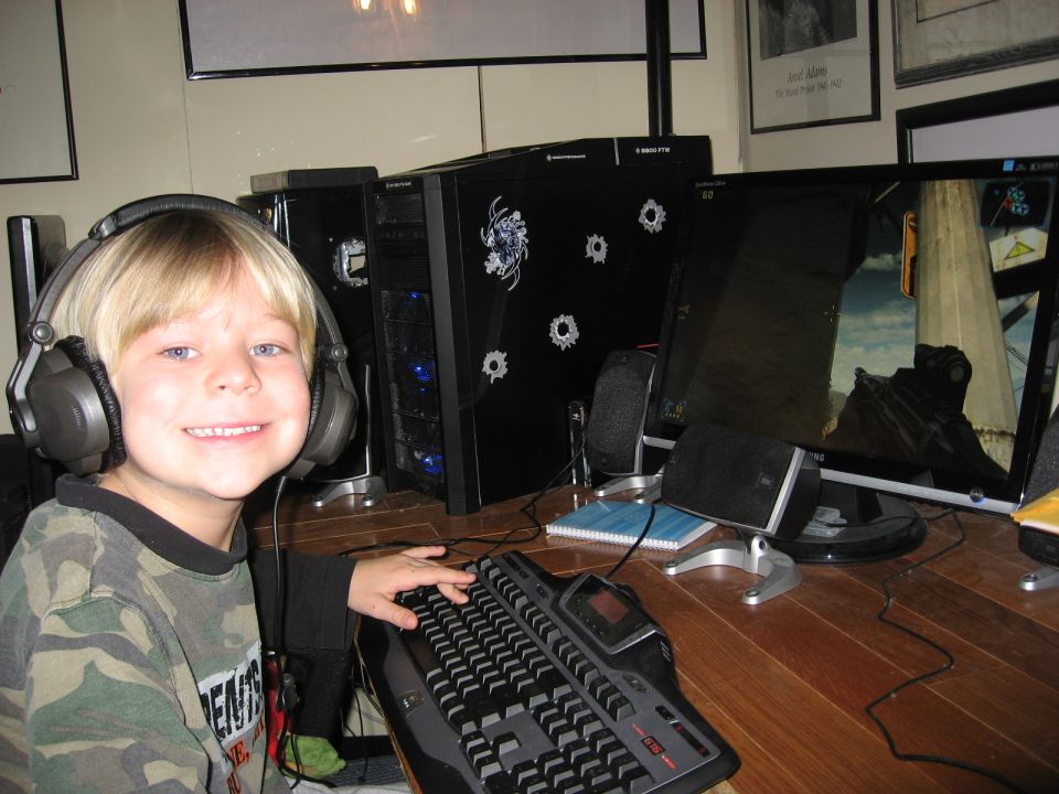 Smiling boy in headphones at a computer desk playing a game