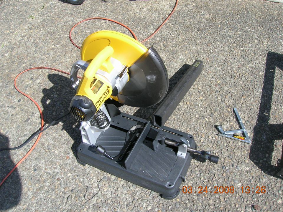 Yellow DeWalt chop saw on a black base, with a piece of square steel stock next to it
