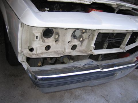 1991 Ford LTD Crown Victoria - The front of a white 1991 Ford Crown Victoria LTD is shown with its hood open, revealing the engine bay and missing headlight assemblies.