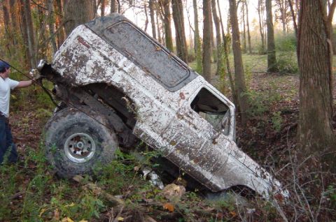 1979 Ford Bronco - A heavily mud-splashed 1978 Ford Bronco is stuck sideways in a wooded area, with a person attempting to pull it free.