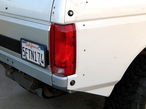 1996 Ford Bronco - Close-up of the driver-side rear corner of a white Ford truck/SUV showing the vertical red-and-clear taillight and a California license pla…