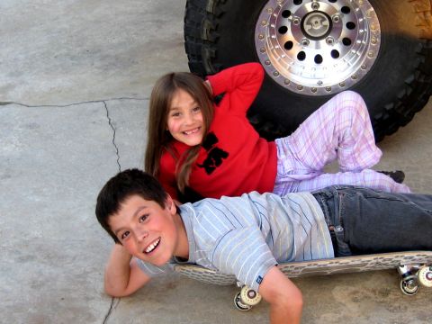 1996 Ford Bronco - Two smiling children lie on the concrete ground beside a large off-road tire mounted on a polished machined aluminum wheel, likely from the…