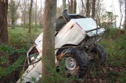 1979 Ford Bronco - A white 1979 Ford Bronco lies crashed on its side amongst trees in a wooded area.