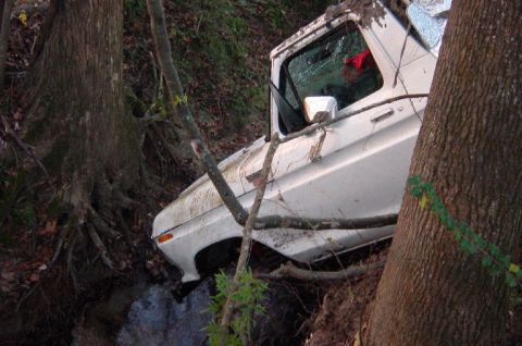 1979 Ford Bronco - A white 1979 Ford Bronco is stuck in a ditch, surrounded by trees and foliage.