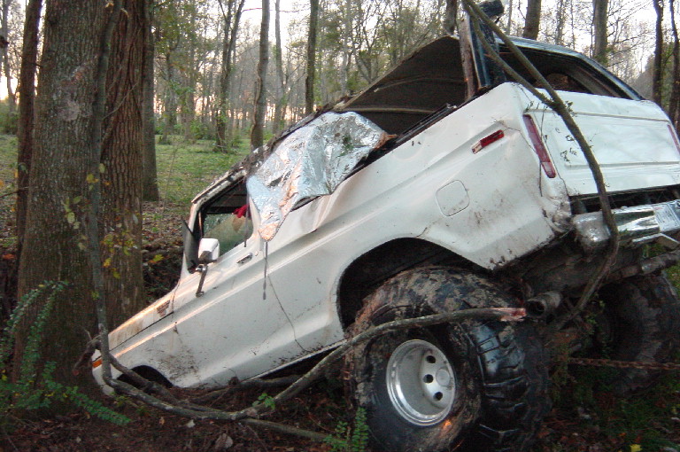 White Ford Bronco crashed nose-down against trees in woods with body damage