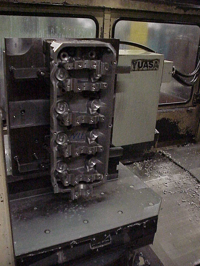 Cast cylinder head clamped in a CNC machine for machining.