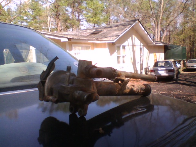 Rusty steering gearbox and shaft resting on a car hood outdoors