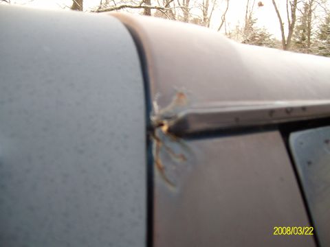 1988 Ford Bronco - Detail of a corroded seam on the roof of a vehicle, with trees visible in the background.