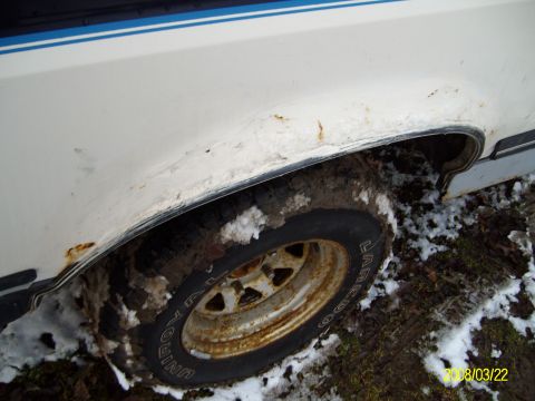 1988 Ford Bronco - This photo shows the rusty wheel well and tire of a white vehicle, partially covered in snow and mud.