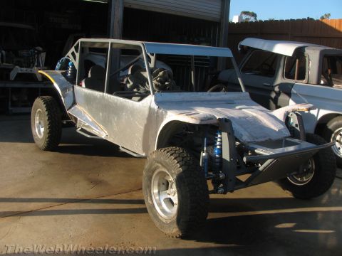 1990 Ford Bronco - bare aluminum-bodied tube-chassis off-road buggy under construction sitting in a workshop yard beside other project vehicles.