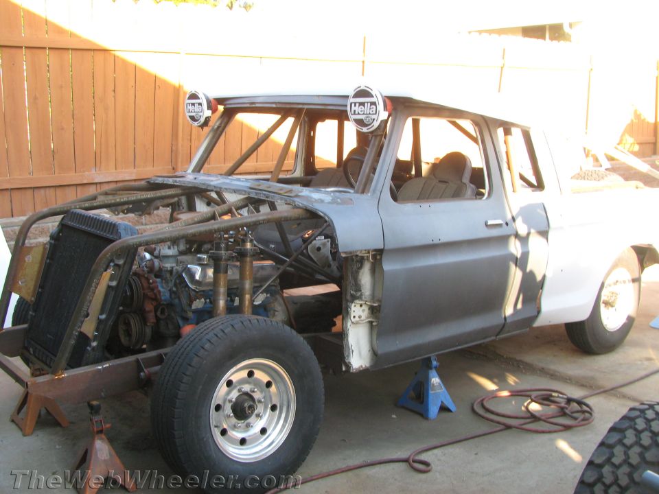 Partly stripped classic pickup cab with engine exposed and roll cage on jack stands