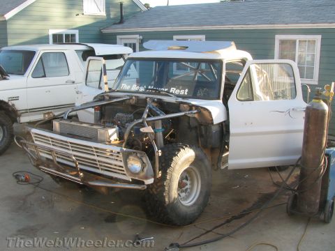 1990 Ford Bronco - white classic Ford truck with its hood open, exposed engine, tube bumper, and welding gas tank nearby during fabrication.