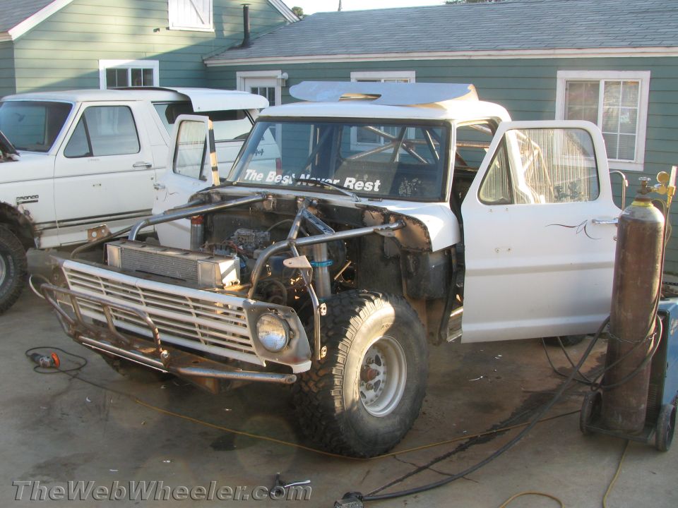 Classic Ford truck with open hood and exposed engine on a driveway during a build