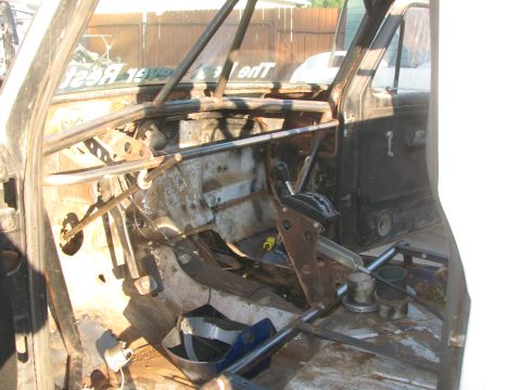 1990 Ford Bronco - Gutted truck cab interior revealing the bare metal floor, pedals, transmission shifter, and surrounding roll cage tubing.