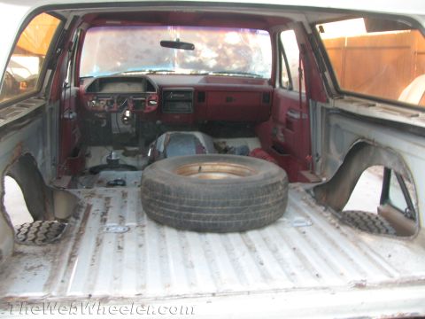 1990 Ford Bronco - View from the rear of a gutted Ford SUV showing the red dashboard, stripped cargo floor, and a spare tire lying inside.