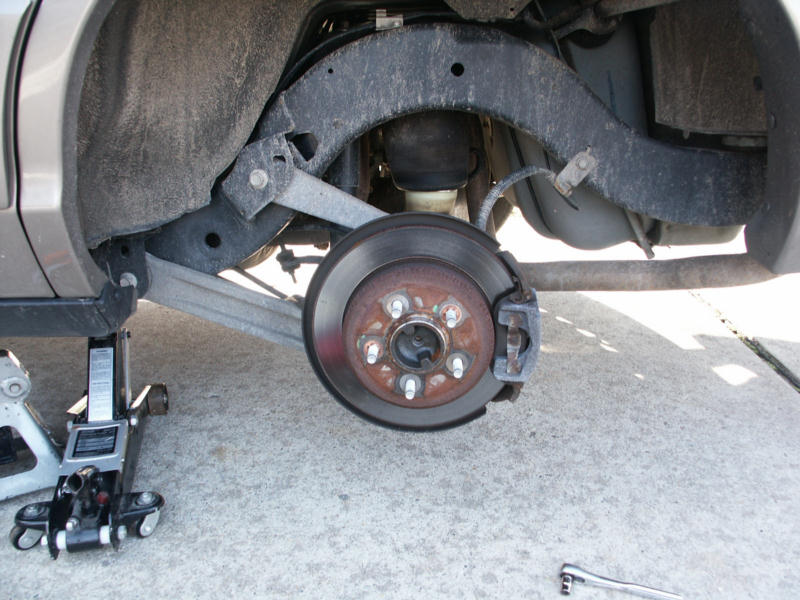 Rear brake rotor and hub exposed with wheel removed, car on a floor jack over concrete