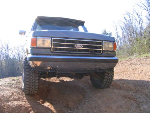 1989 Ford Bronco - This Ford truck, likely from the late 1980s, is shown from a low front angle on a dirt path.