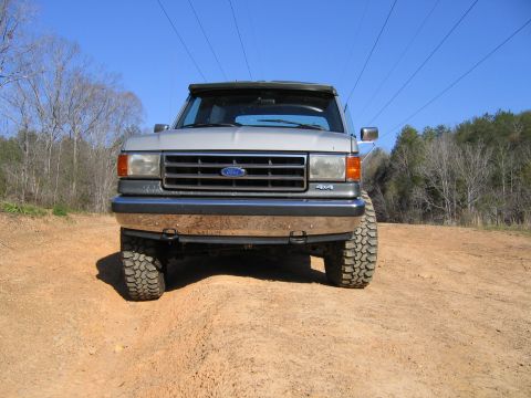 1989 Ford Bronco - A silver Ford Bronco is seen from the front on a dirt road with trees in the background.