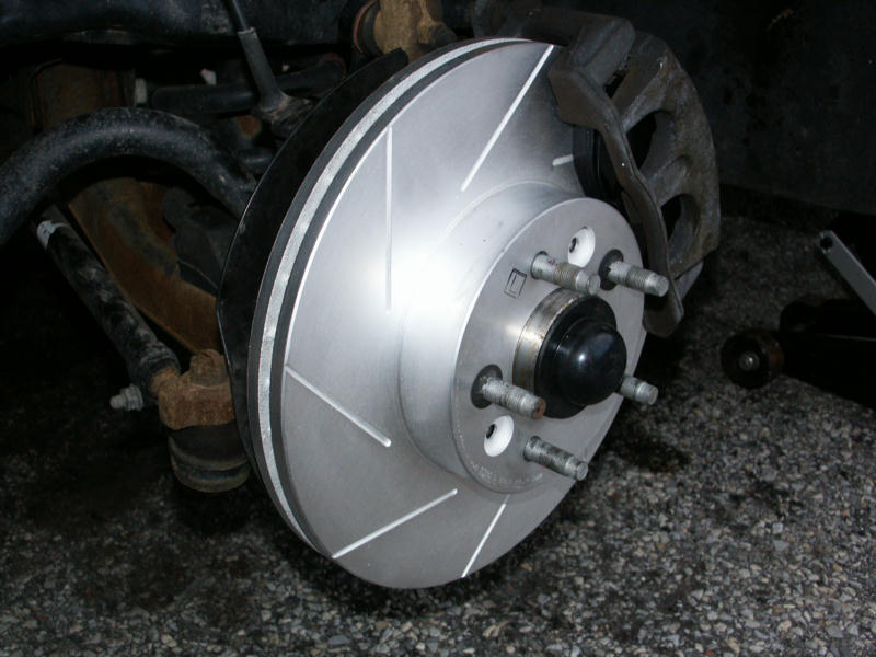 New slotted brake rotor installed on front hub with wheel removed, caliper visible behind