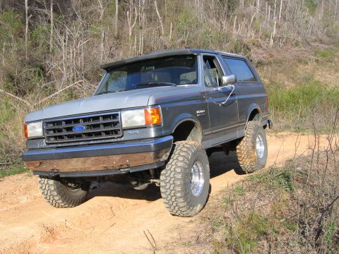 1989 Ford Bronco - This lifted Ford Bronco navigates a dirt trail with its large tires kicking up dust.