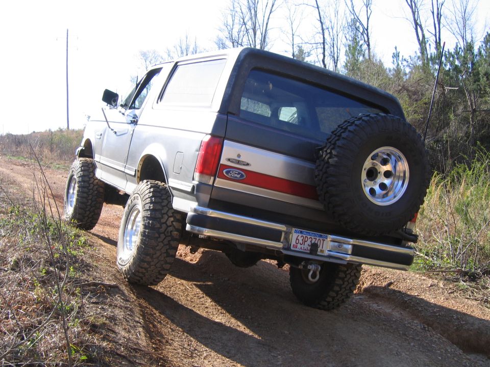 1989 Ford Bronco with spare tire mounted on rear, driving on dirt road